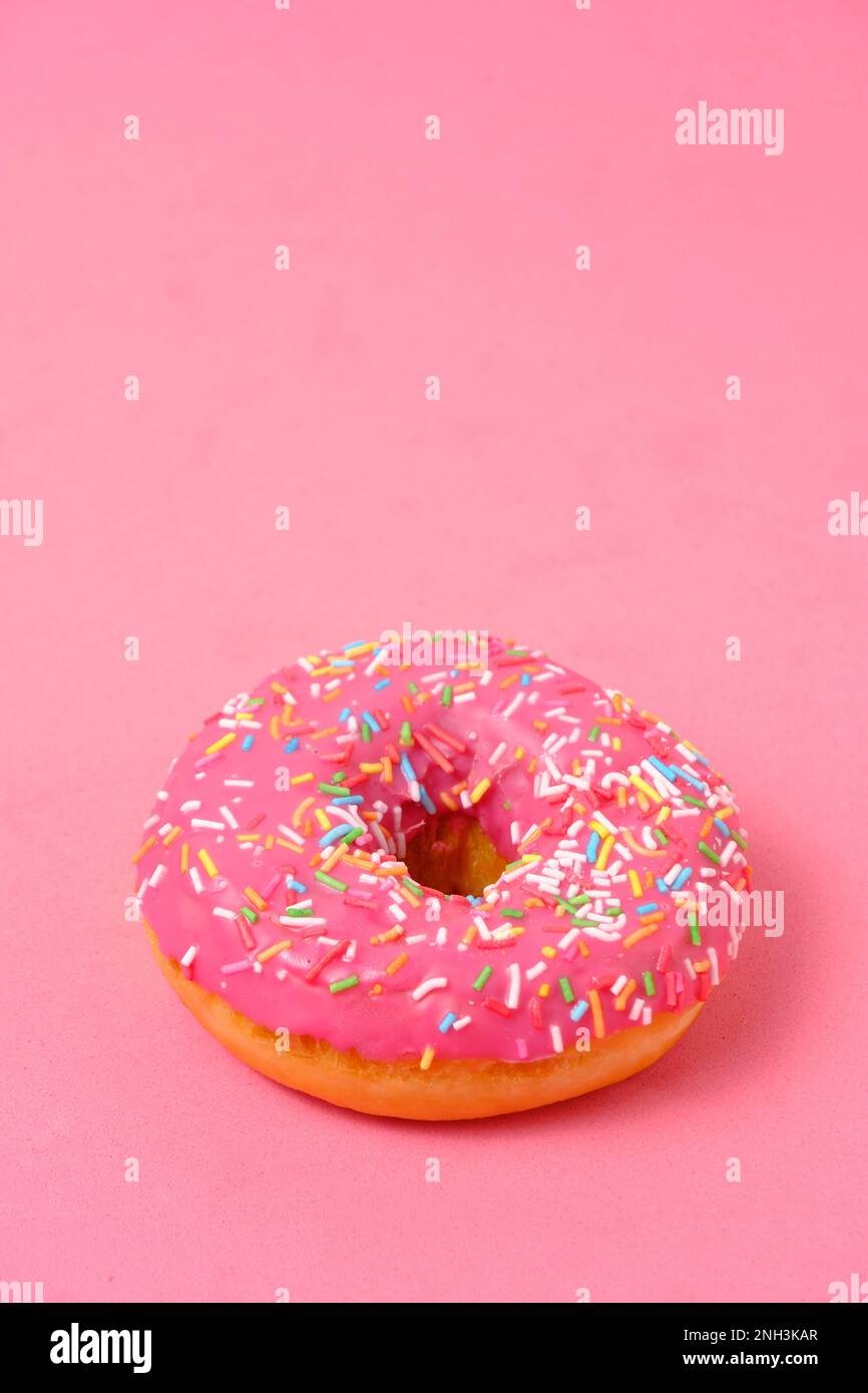 Donut mit pinkfarbenem Glasur und bunten Zuckerstreuseln. Auf pinkfarbenem Hintergrund Stockfoto