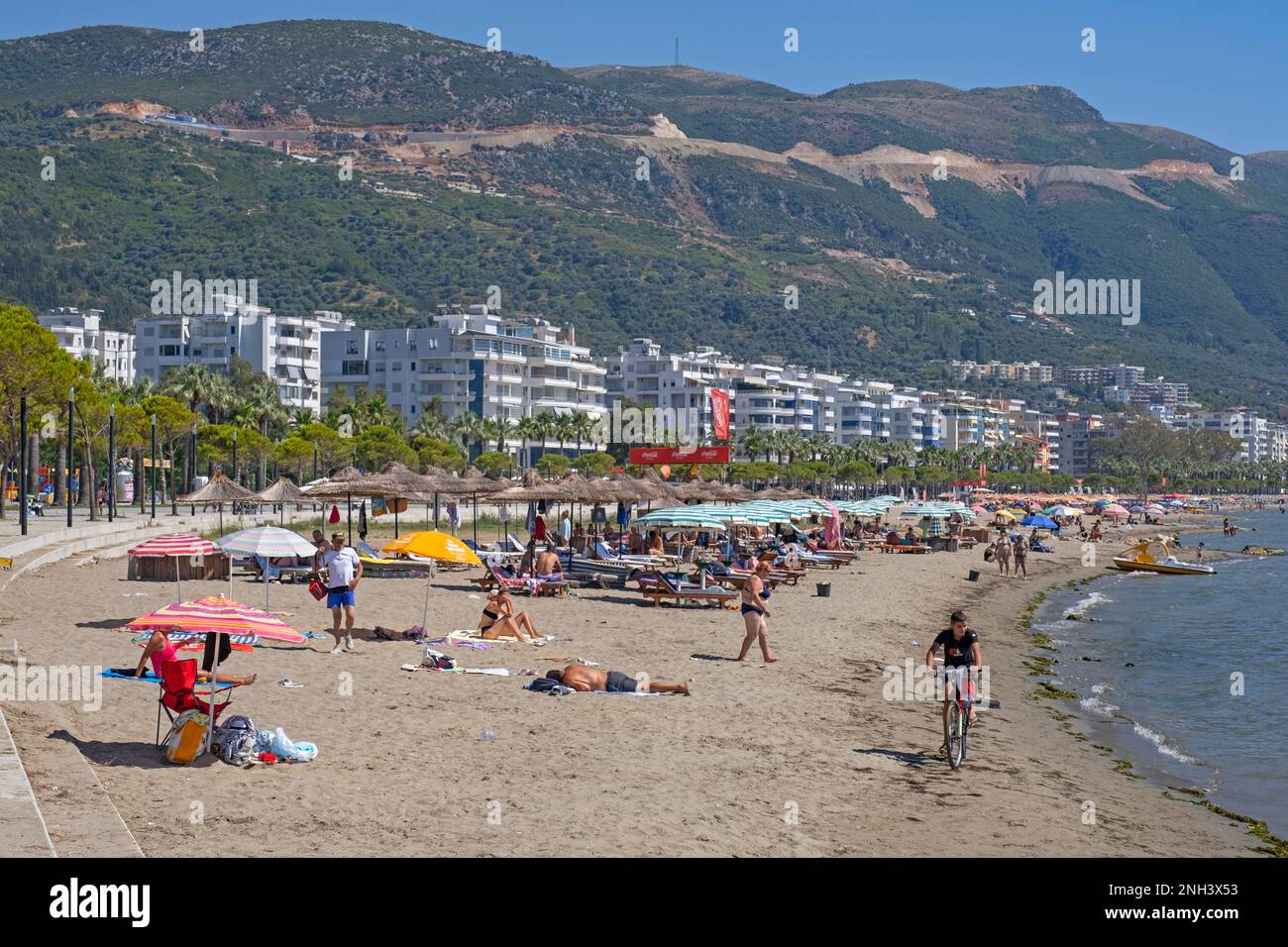 Sonnenanbeter am Sandstrand entlang der Bucht von Vlorë im Sommer und der Ceraunian Mountains im Hinterland von Vlora im Südwesten Albaniens Stockfoto