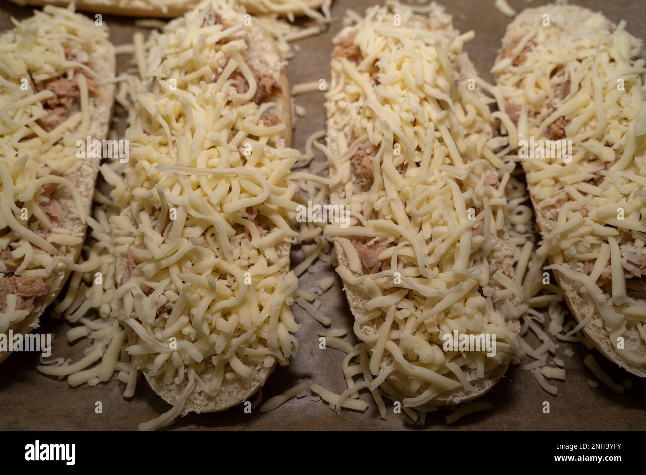 Ungebackene Thunfisch-Sandwich-Hälften mit Käse auf dem Backblech Stockfoto
