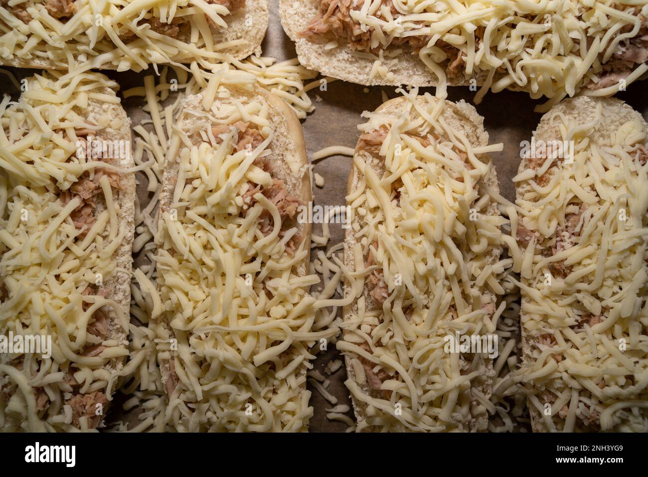 Draufsicht auf halbierte, ungebackene Sandwiches auf dem Backblech, garniert mit Thunfisch und Käse Stockfoto