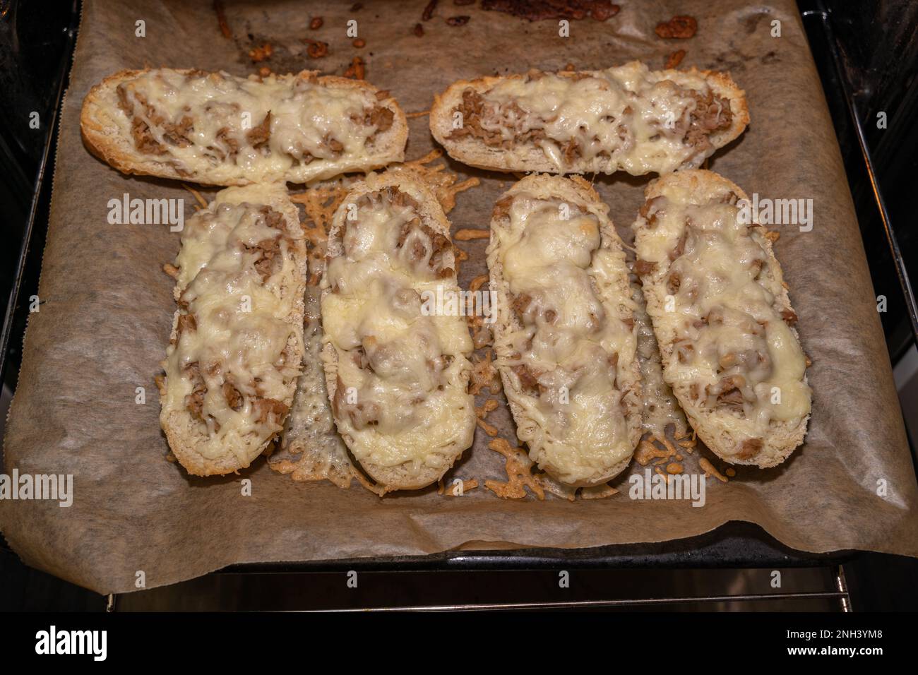Knusprig gebackene Thunfischsandwiches mit geschmolzenem Käse auf einem Backblech mit Pergamentpapier Stockfoto