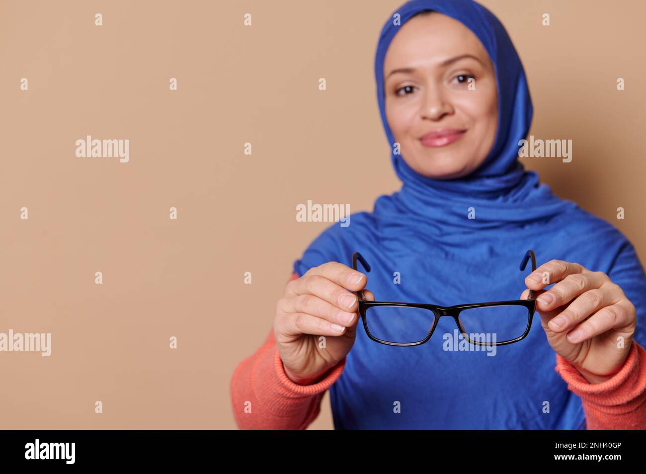 Selektiver Fokus auf schwarze Brillen - Brille in den Händen stilvoller muslimischer Frauen, isoliert auf beigem Hintergrund Stockfoto