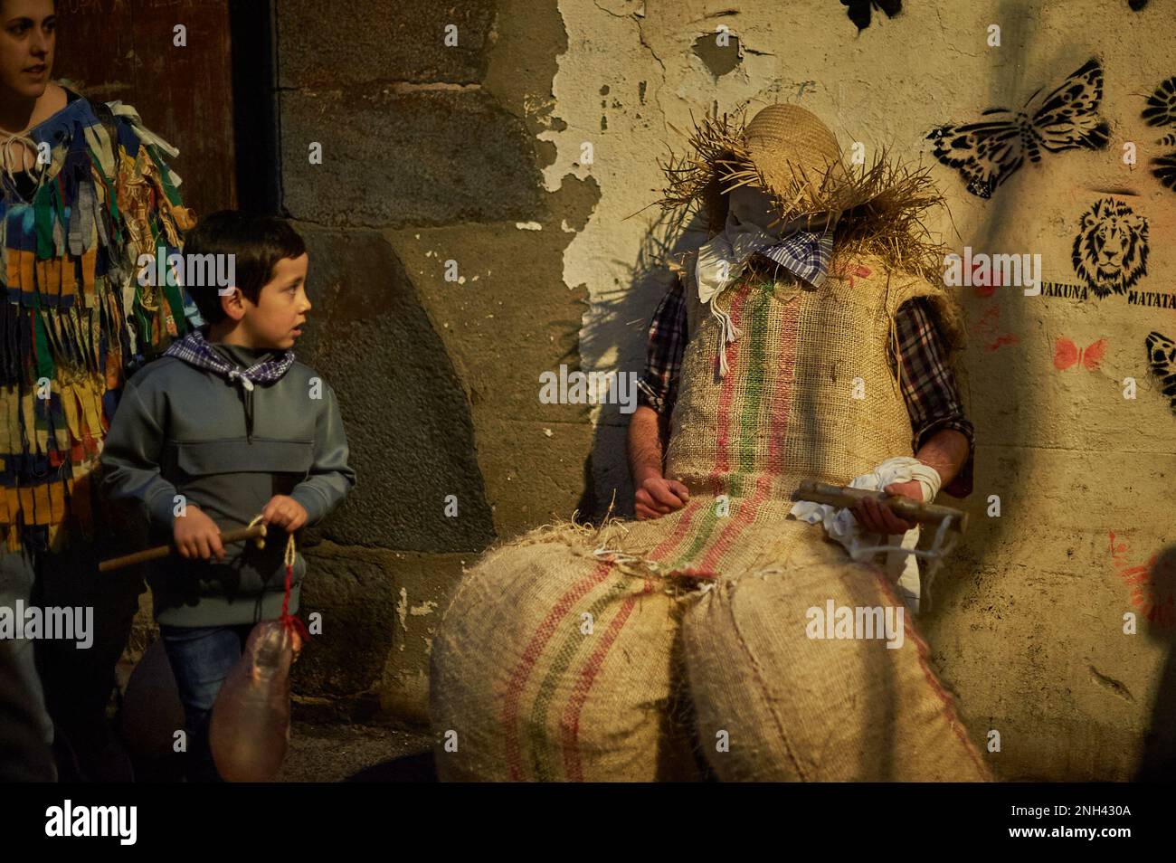 Lesaka, Spanien. 19. Februar 2023. Ein Kind schaut auf einen „zaku-zaharrak“, während er auf der Wand eines Hauses ruht, bevor die Tour während des Karnevals von Lesaka beginnt. Der „zaku-zaharrak“ sind typische Figuren des Lesakakaker Karnevals, gefüllt in Säcke voller Stroh mit Gesichtern bedeckt mit Schals, die aufgeblasene Blasen tragen, um die Menschen zu treffen, die bei Sonnenuntergang durch die Straßen der Stadt laufen. (Foto: Elsa A Bravo/SOPA Images/Sipa USA) Guthaben: SIPA USA/Alamy Live News Stockfoto