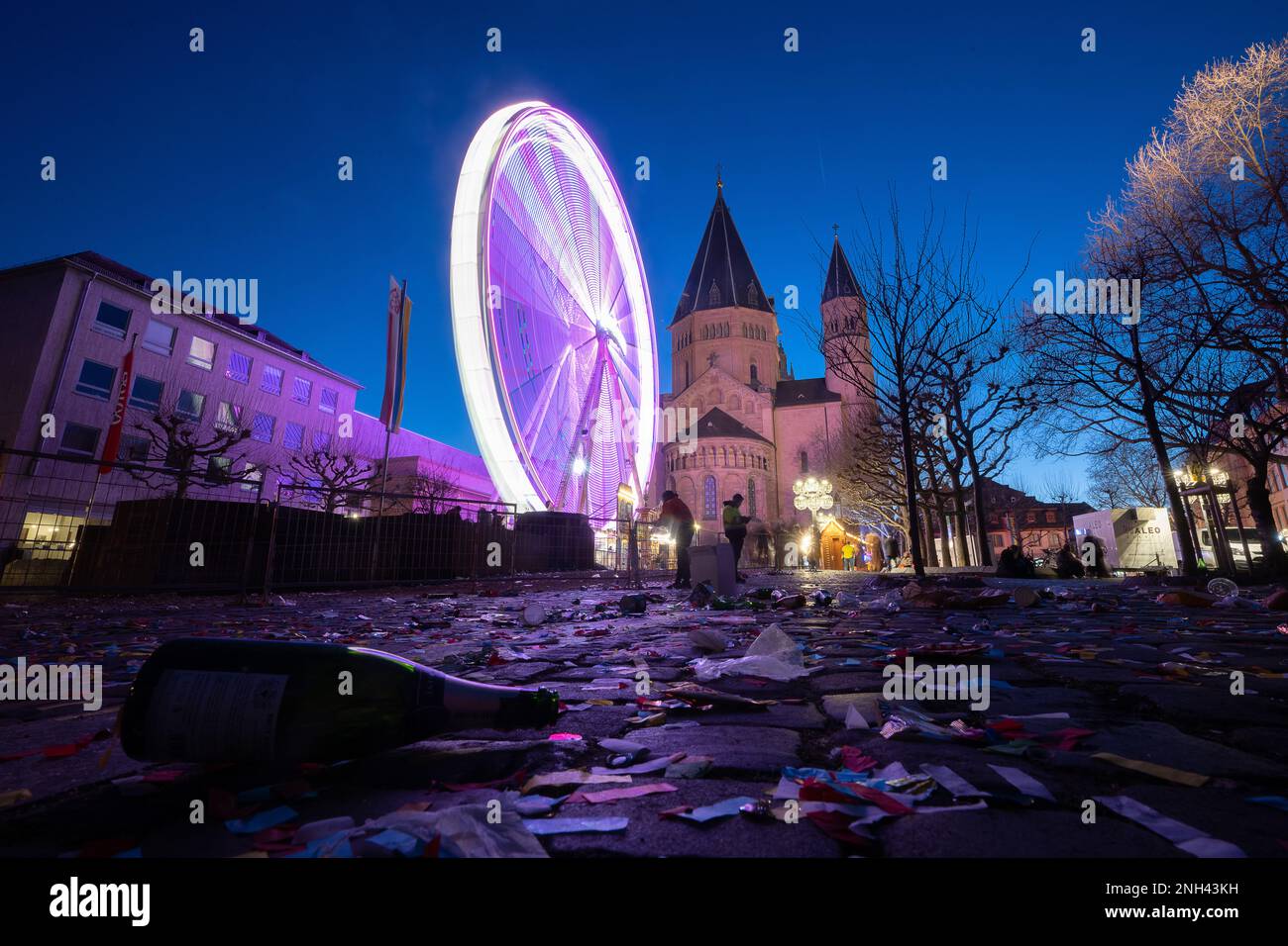 Mainz, Deutschland. 20. Februar 2023. Ein Riesenrad dreht sich nach der Shrove-Montags-Prozession vor der Kathedrale, während eine Flasche im Vordergrund liegt. Das Motto der Prozession lautete: "In Mainz steht Shrovetide voll und ganz für Frieden, Freiheit, Toleranz!" Aufgrund der Corona-Pandemie fand sie zum ersten Mal seit zwei Jahren statt. Kredit: Sebastian Christoph Gollnow/dpa/Alamy Live News Stockfoto