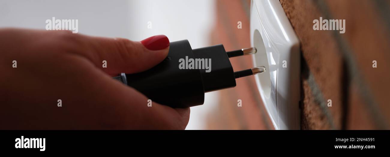 Erwachsene Frau hält sich in den Händen und verbindet schwarzen Stecker mit Steckdose zu Hause Stockfoto