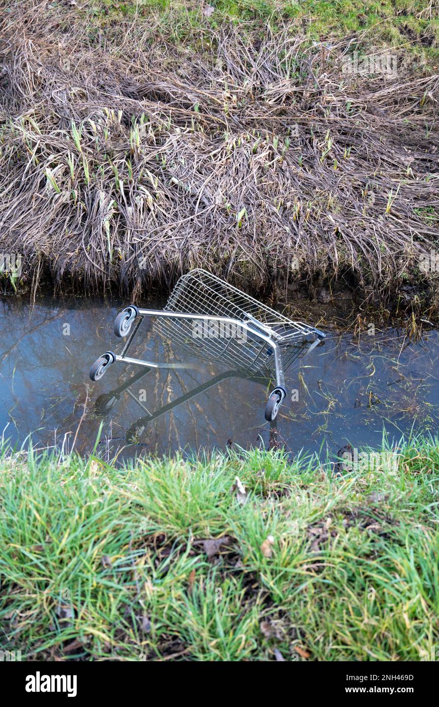 Ein Supermarkt-Einkaufswagen, der in einen Wassergraben geworfen wurde und Müll und Umweltschäden verursachte. Stockfoto