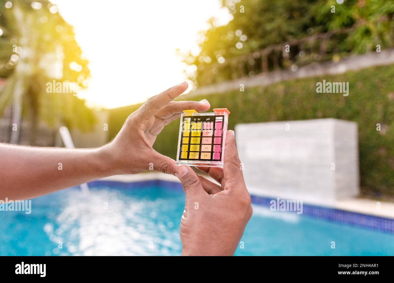Hand hält einen pH-Wert- und Chlortester, Hand zeigt Wassertestkit mit Hintergrund des Schwimmbeckens. Wartungspersonal mit einem Pool-ph und Stockfoto