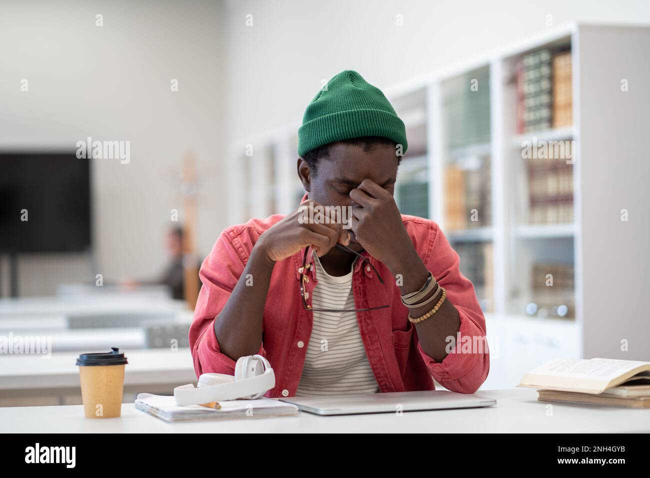 Gestresster, müder schwarzer Schüler fühlt sich erschöpft, wenn er im Klassenzimmer nach dem Laptop-Netzwerk sitzt. Stockfoto
