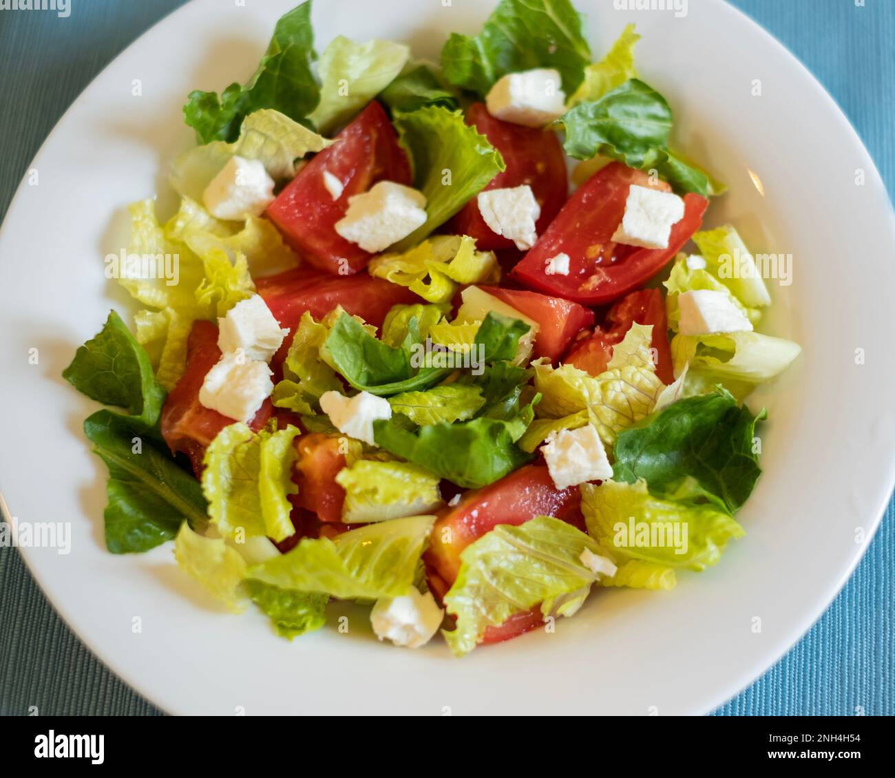 Ein frischer Salat mit Römersalat, geschnittenen Tomaten und Fetakäse in einer weißen Schüssel. Nahaufnahme, von oben. Stockfoto