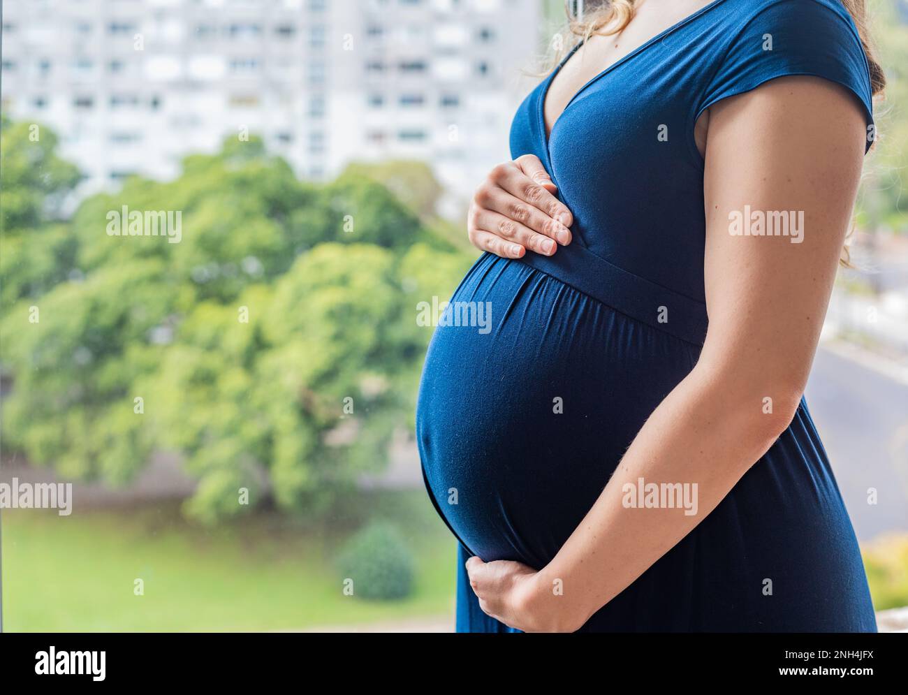 Schwangere Frau, die ihren Bauch vor einem Stadtbild hält Stockfoto