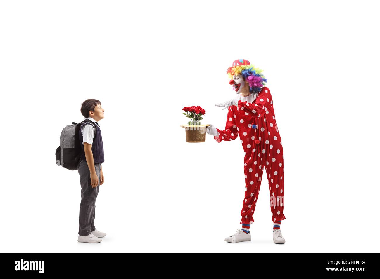 Ein Schuljunge, der einem Clown zusieht, der einen Trick mit Hut und Blumen auf weißem Hintergrund vorführt Stockfoto