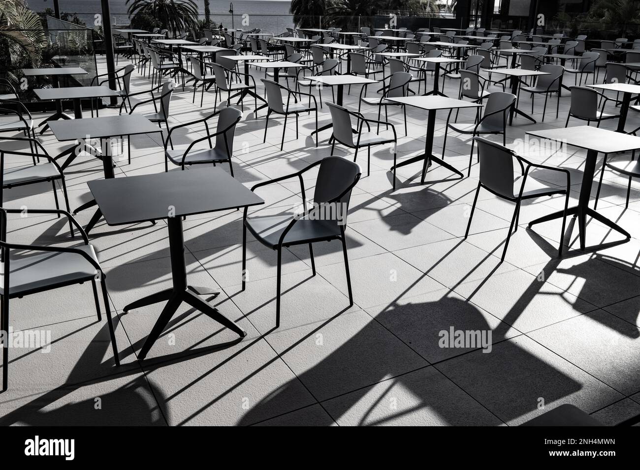 Schwarze Tische und Stühle in hellem Sonnenlicht werfen lange Schatten Stockfoto