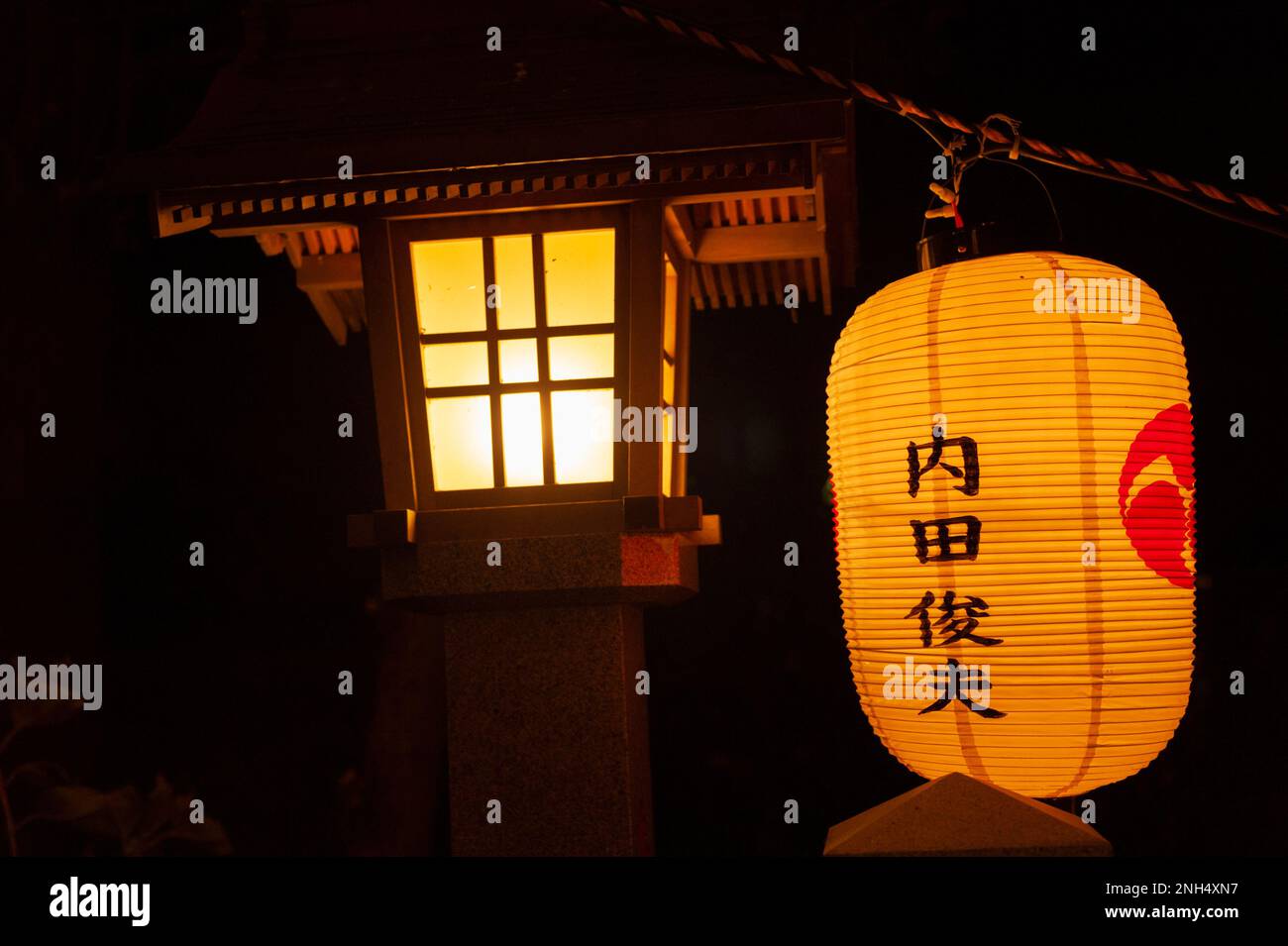 Eine Steinlaterne und eine Papierlaterne (mit dem Namen der Sponsoren) leuchteten zu Silvester in einem Shinto-Schrein in Yokohama, Japan. Stockfoto