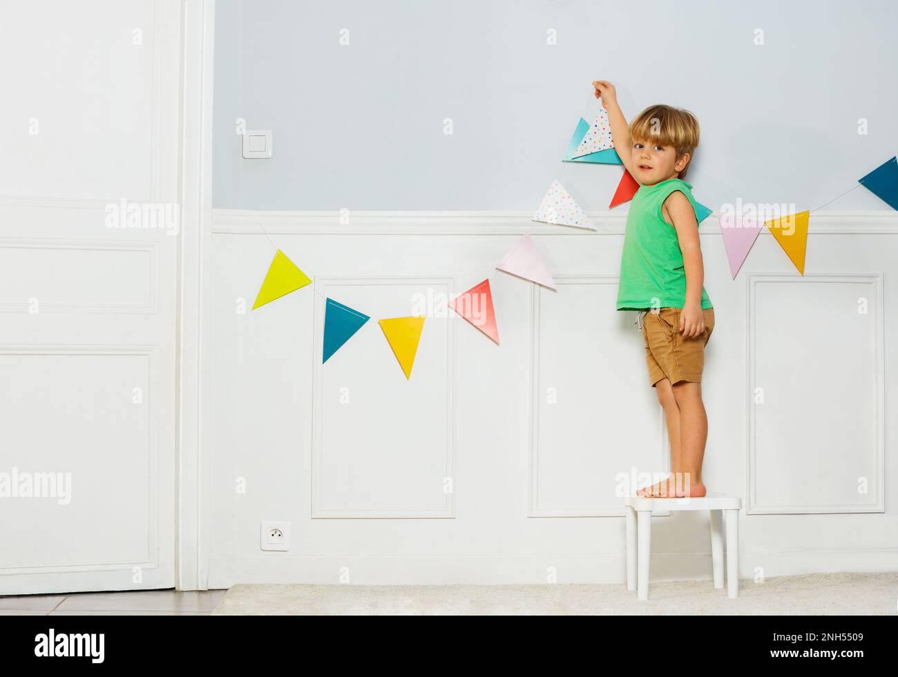 Der kleine Junge schmückt das Wohnzimmer mit Geburtstagsparty-Wimpeln Stockfoto