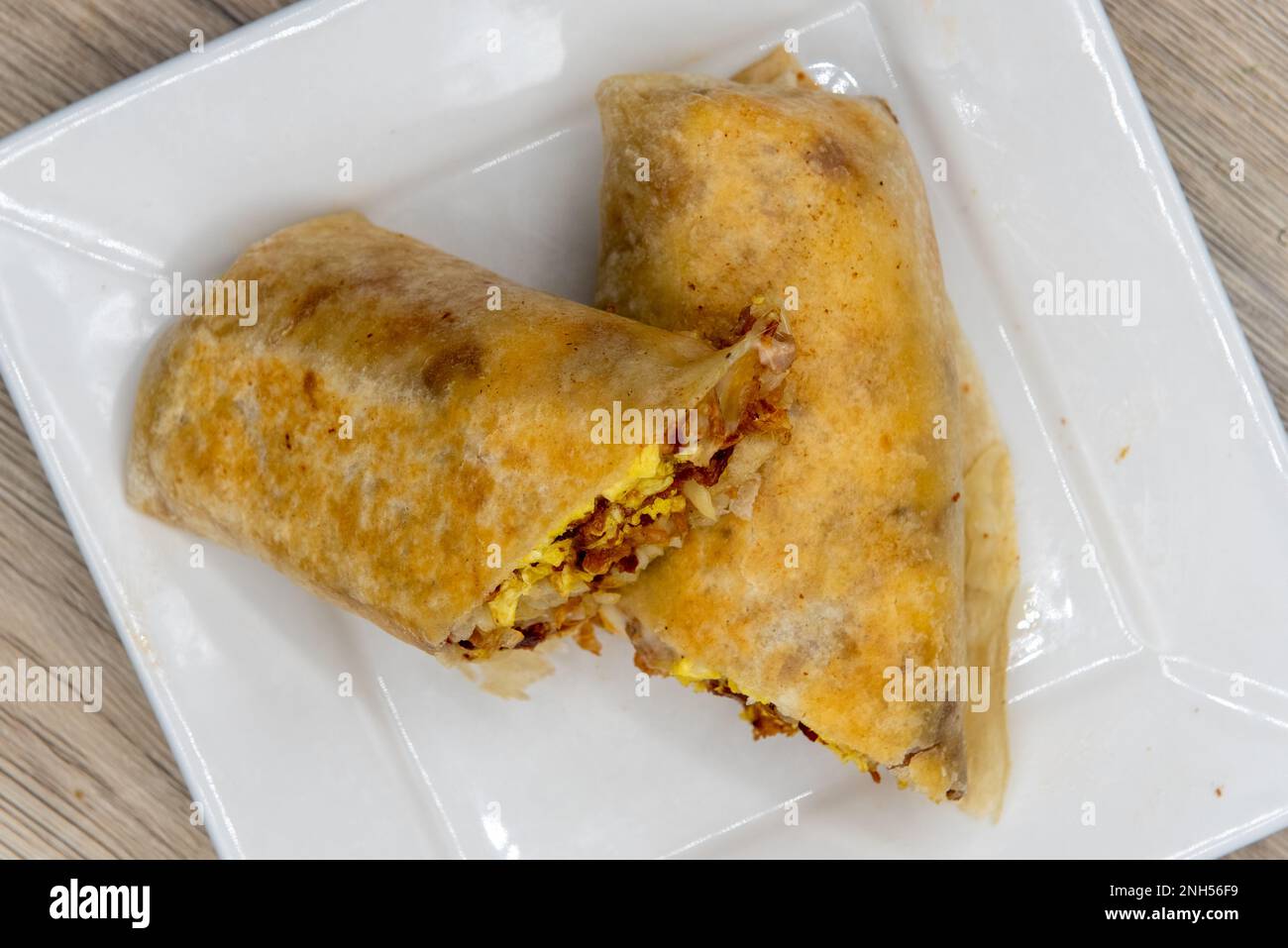 Blick von oben auf den traditionellen Frühstücks-Burrito mit Eiern, Kartoffeln, Salsa und Käse, alles verpackt in einer gegrillten Mehltortilla zum Essen. Stockfoto