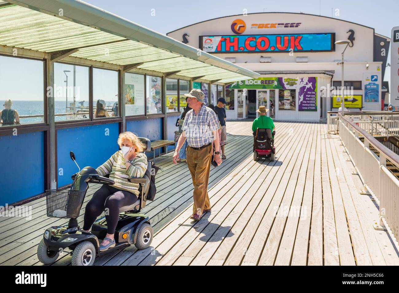BOURNEMOUTH, Großbritannien - 08. Juli 2022. Ältere Ehepaare machen einen Spaziergang am Bournemouth Pier, mit einer Frau auf einem Roller. Alter und Behinderung Stockfoto