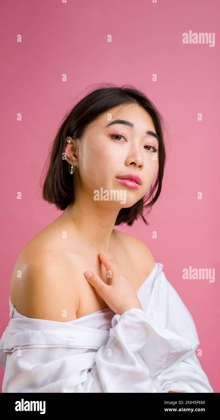 Nahaufnahme einer jungen asiatischen Frau mit kurzer weißer Bluse auf pinkfarbenem Hintergrund | Make-up | Mode Stockfoto