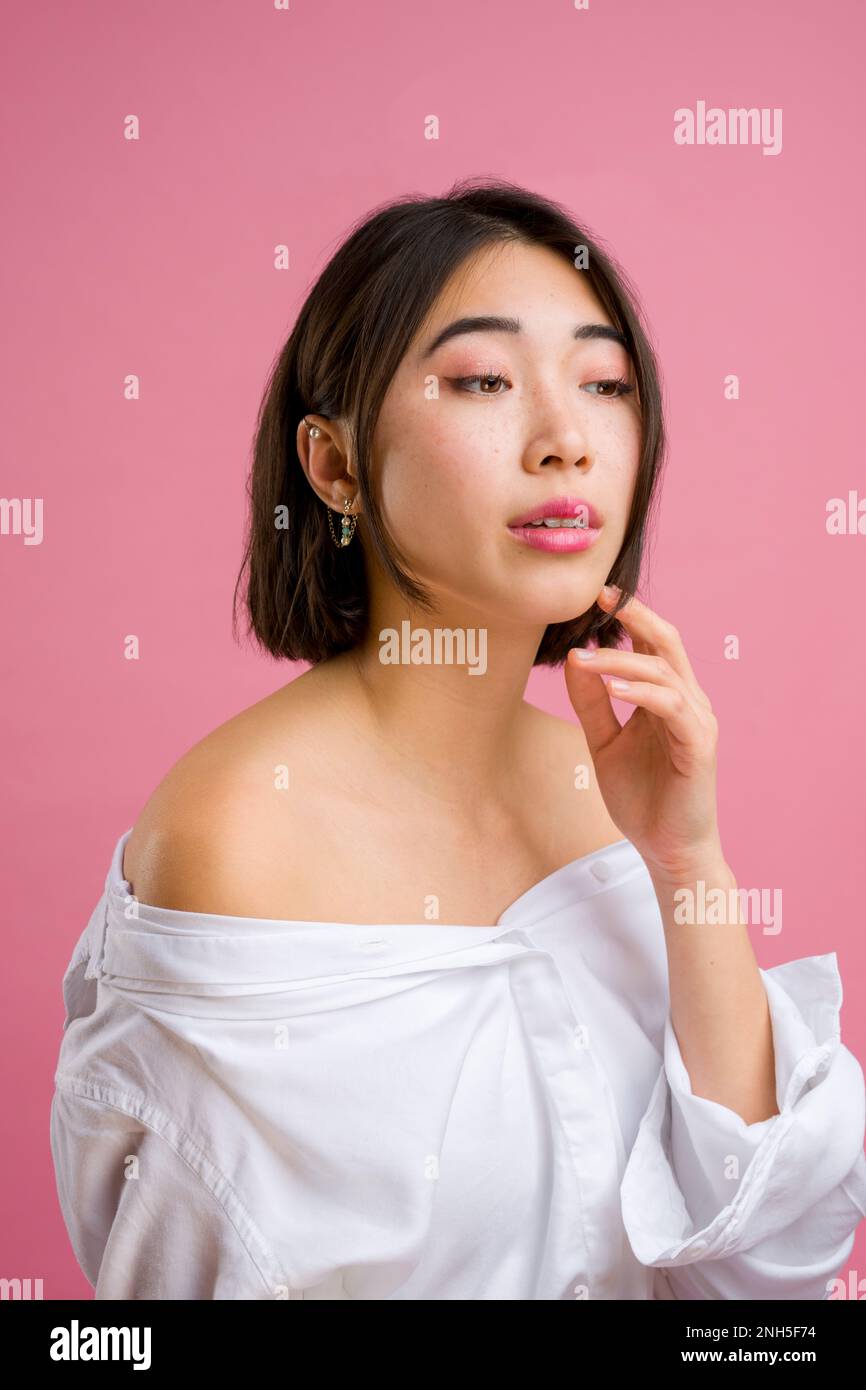 Nahaufnahme einer jungen asiatischen Frau mit kurzer weißer Bluse auf pinkfarbenem Hintergrund | Make-up | Mode Stockfoto