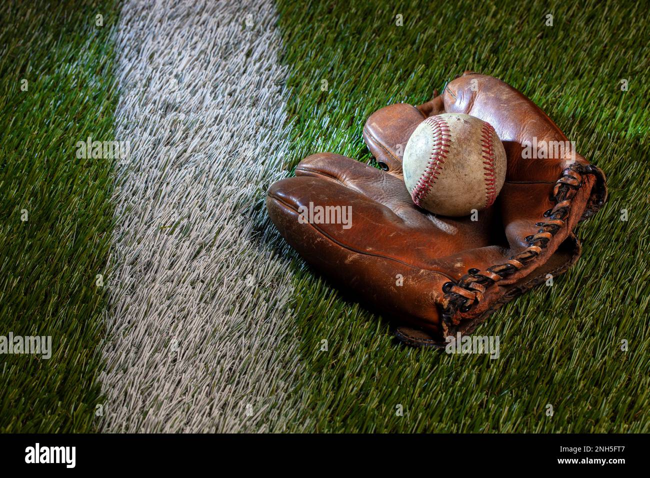 Alter Baseball mit braunem Lederhandschuh auf einem Rasenfeld mit weißem Streifen Stockfoto