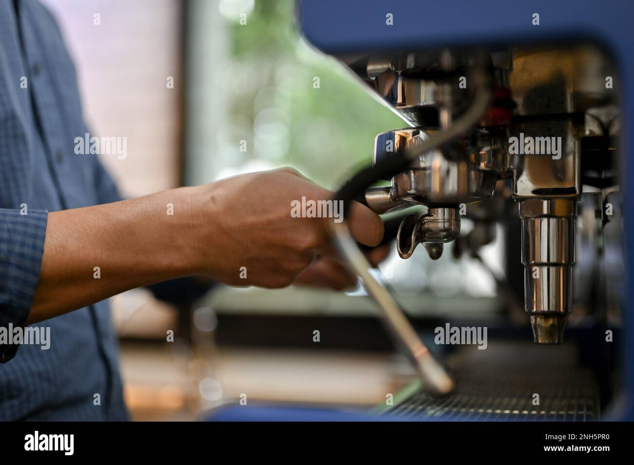 Ein männlicher Barista, der einen Portafilter verwendet, um einen Espresso Shot mit einer Espressomaschine zuzubereiten, ein Kaffeegetränk für einen Gast zuzubereiten, im Café zu arbeiten. Gekürzt Stockfoto
