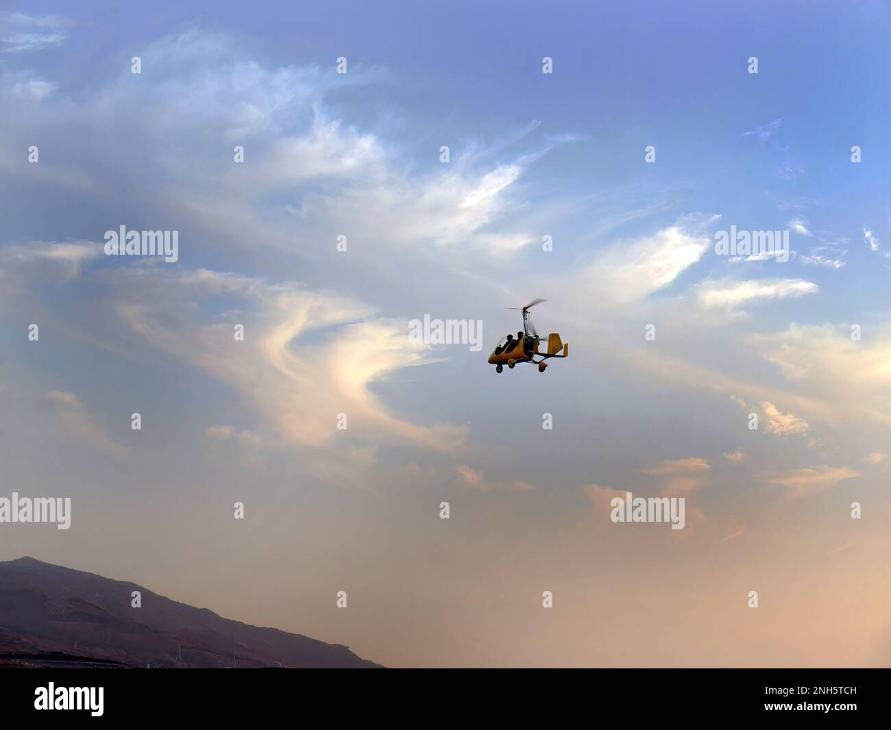 Tiefer Winkel, gelber Gyrocopter, der im blauen Himmel fliegt und dramatische Wolken, lustige Fliege, Flugsport, Fallschirmsprung, Roto Craft, Gyroplane, Fallschirmspringen, Stockfoto