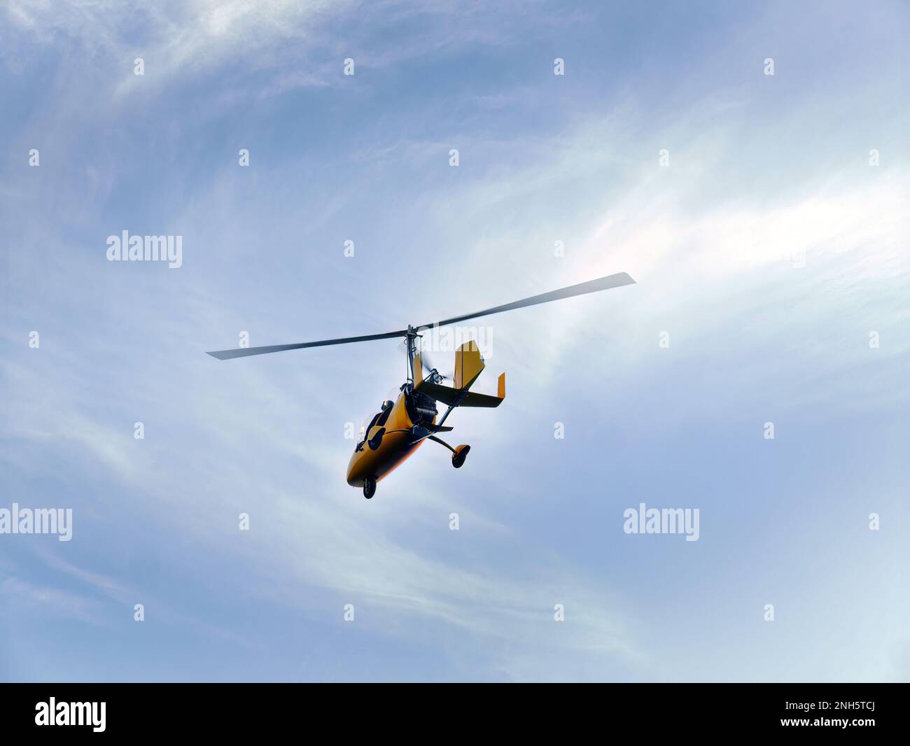 Tiefer Winkel, gelber Gyrocopter, der im blauen Himmel fliegt und dramatische Wolken, lustige Fliege, Flugsport, Fallschirmsprung, Roto Craft, Gyroplane, Fallschirmspringen, Stockfoto