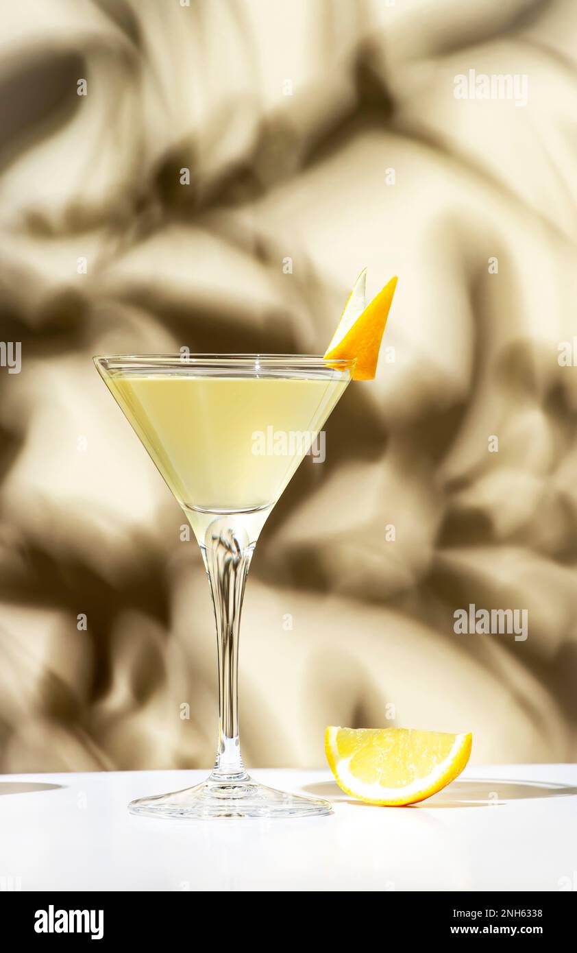 Vesper, klassisches alkoholisches Cocktailgetränk mit trockenem Gin, Wodka, Aperitif, Zitronenschale und Eis. Hellbeiger Hintergrund, hartes Licht, Schattenmuster Stockfoto