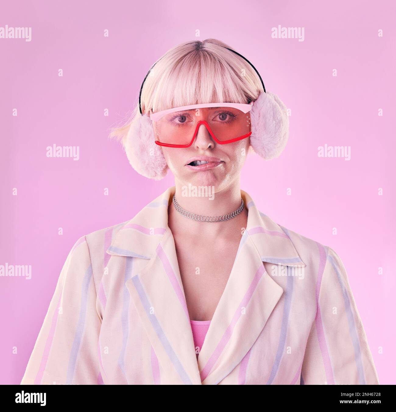 Mode, Eigenart und Porträt einer Frau im Studio mit lustigem oder komischem Gesicht auf pinkfarbenem Hintergrund. Ästhetischer Modellmann mit Brille und Ohrenschützer für Edgy Stockfoto
