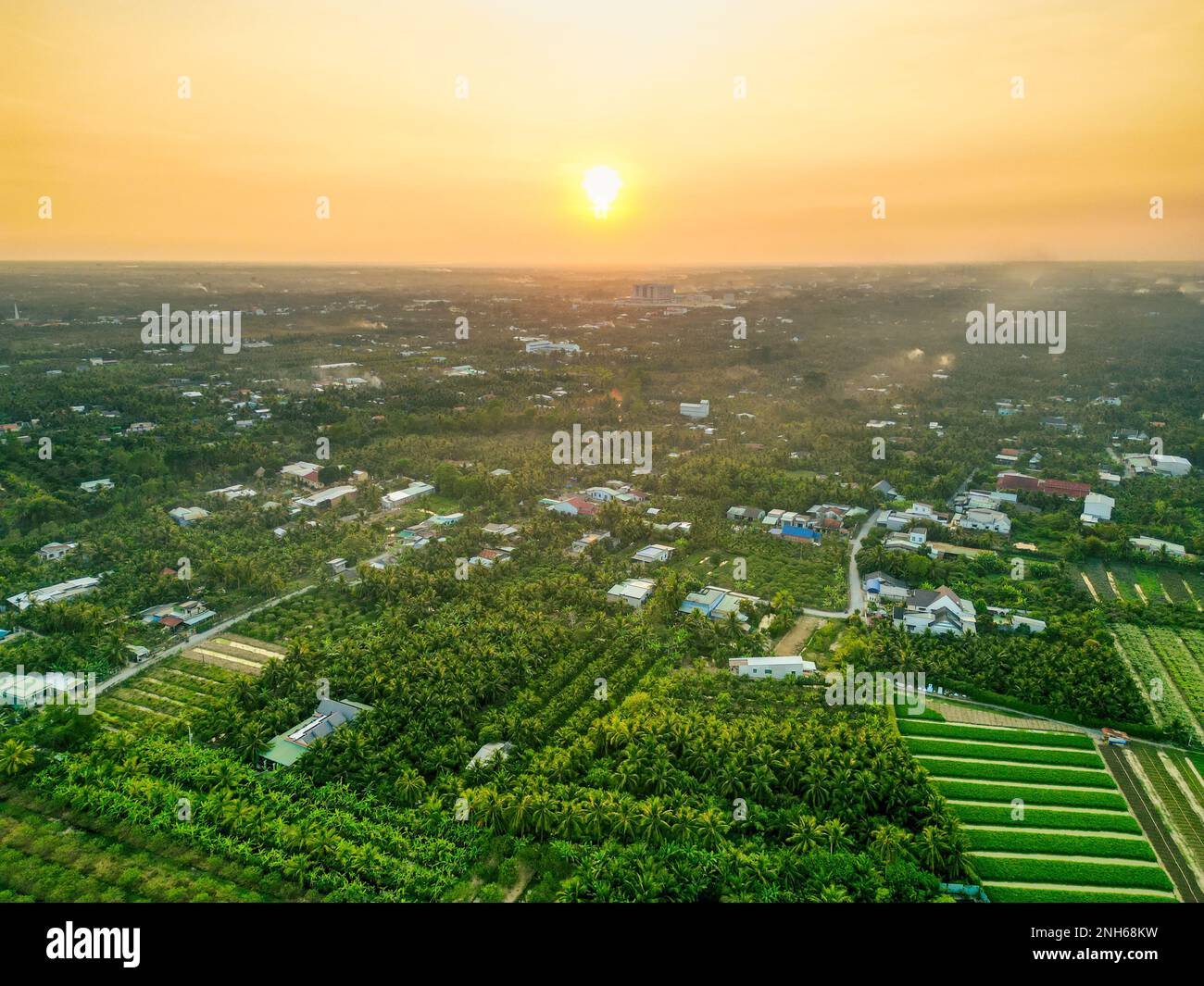 Golden Hour Magic: Atemberaubender Sonnenuntergang über den Feldern der Provinz Tien Giang mit dem ruhigen Fluss und der Stadtlandschaft in Vietnam Stockfoto