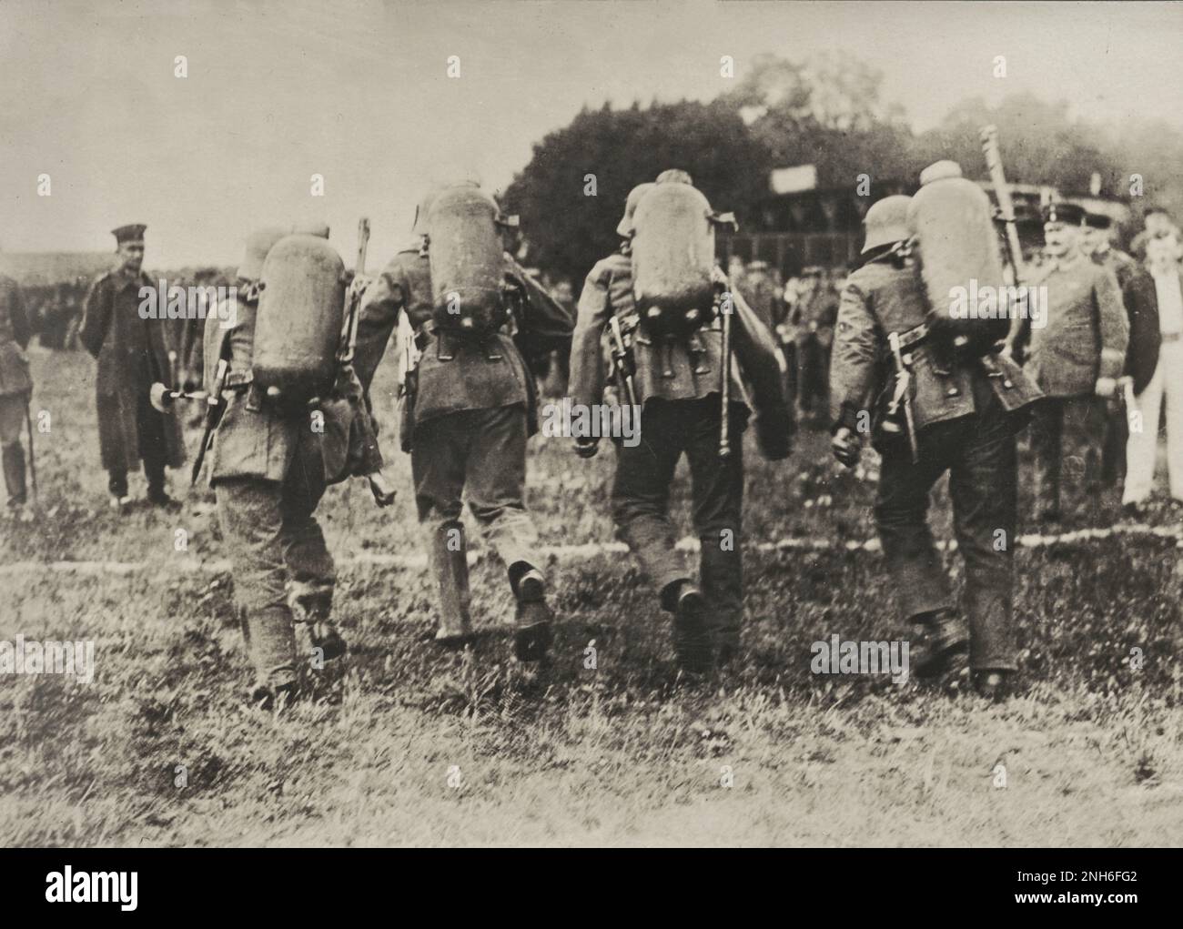 1914-1918. Der 1. Weltkrieg. Vier deutsche Soldaten, komplett ausgestattet mit Uniform, Stahlhelm und Flammenwerfer auf dem Rücken, die ein Rennen führen. Man kann die Männer von hinten sehen, kurz vor der Ziellinie. Im Hintergrund und an den Seiten sind sichtbare Zuschauer. Stockfoto