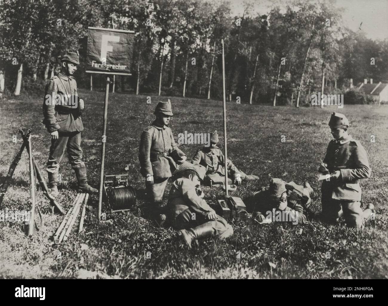 1914-1918. Erster Weltkrieg Eine Gruppe österreichischer Soldaten liegt auf einem Rasen, wo sie eine Mobiltelefonstation eingerichtet haben. Das Schild „Fernsprecher“ bezieht sich auf das Vorhandensein eines Telefons. Einer der Männer liegt auf dem Bauch und redet über seine Kopfhörer, während er schreibt. Auf der linken Seite sehen Sie eine Seiltrommel und drei Gewehre. Stockfoto