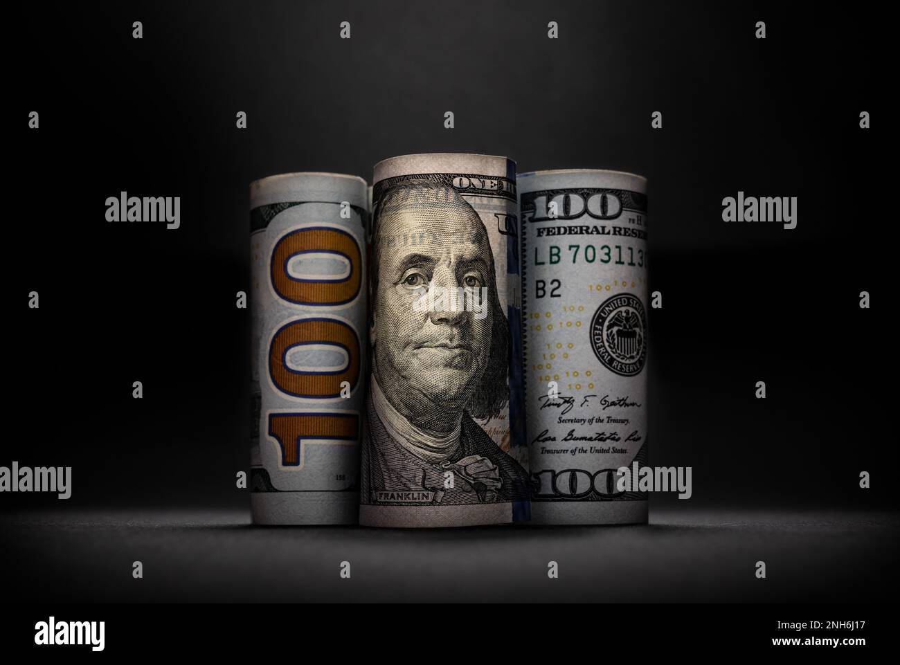 Drei verschiedene Bilder von 100 US-Dollar in Rollen auf dunklem Hintergrund Stockfoto