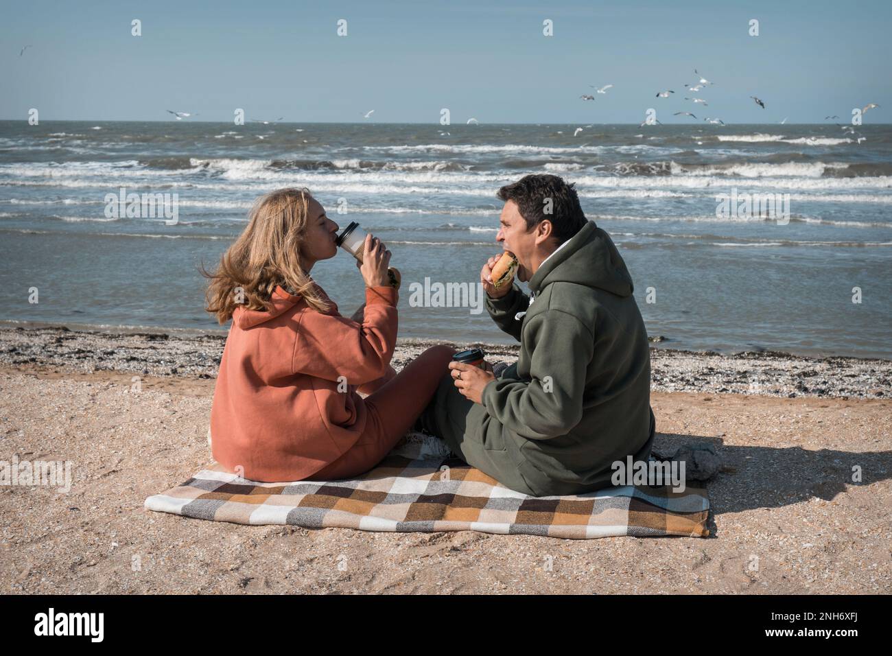 Der Typ und das Mädchen umarmen sich und sehen sich liebevoll am Strand an, vor dem Hintergrund des Blauen Meeres. Das zarte Verhältnis von Mann und Frau. Das Datum des jungen Paares am Valentinstag. Hochwertiges Foto Stockfoto