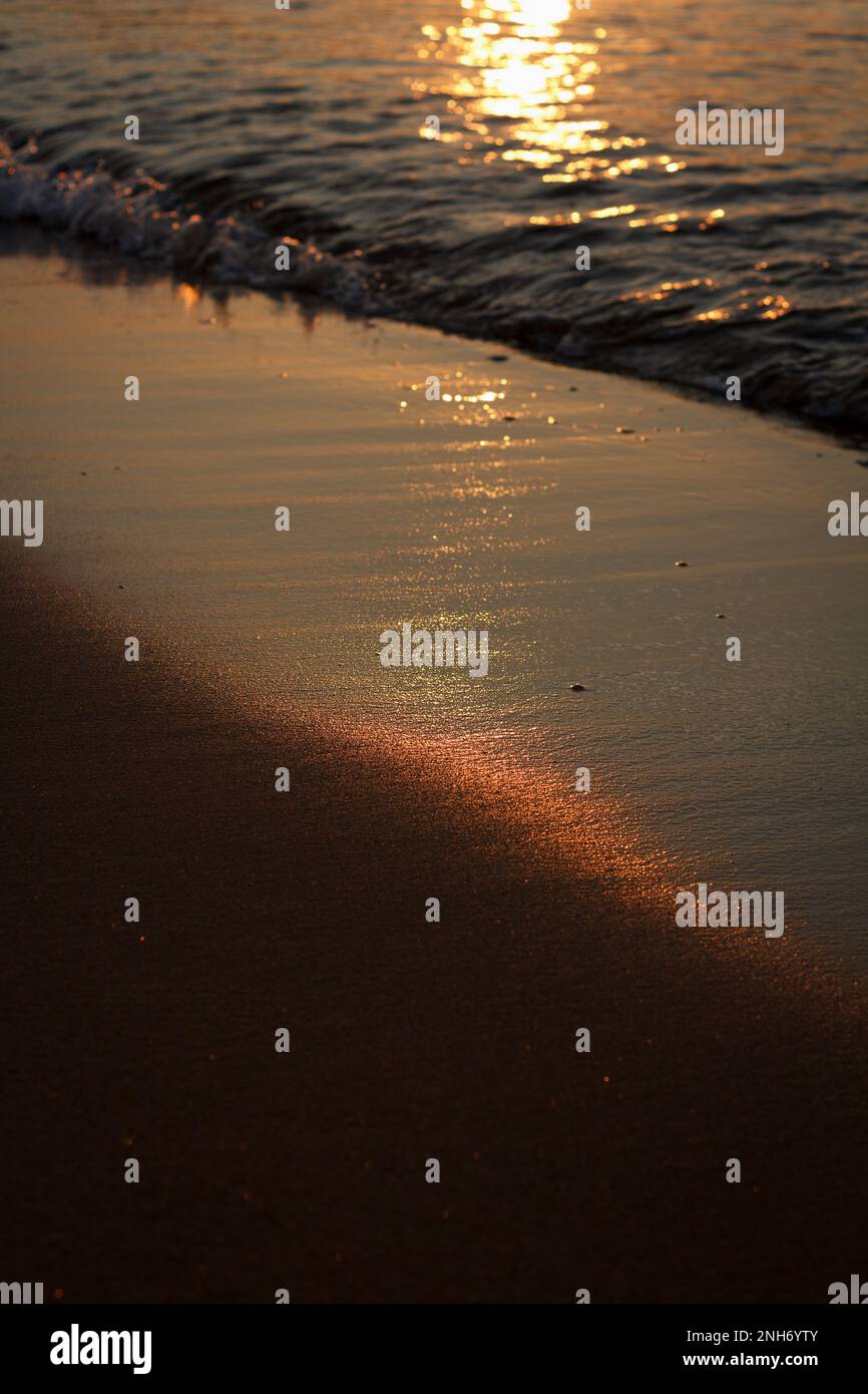 Im Frühsommer geht die Sonne auf das Meer zu, und die ersten Sonnenstrahlen spiegeln sich in Wellen des schwarzen Meeres und nassem Sand an der Küste wider. Schönheitshintergrund Stockfoto