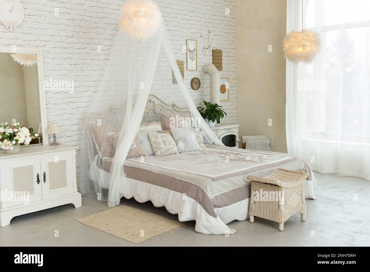 Komfortables, großes, einfaches Schlafzimmer mit hellen Möbeln, Himmelbett, Federlampen, kleinem Kamin auf Holz, gemütlichem, modernem Platz zum Ausruhen und Stockfoto