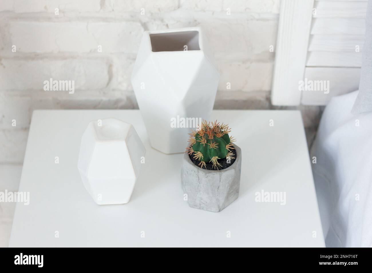 Eine Zimmerpflanze aus der Kaktusfamilie, in einer grauen Vase gepflanzt, liegt auf einem Nachttisch neben einem Kerzenhalter und einer Vase. Diese Artikel lassen sich gut kombinieren w Stockfoto