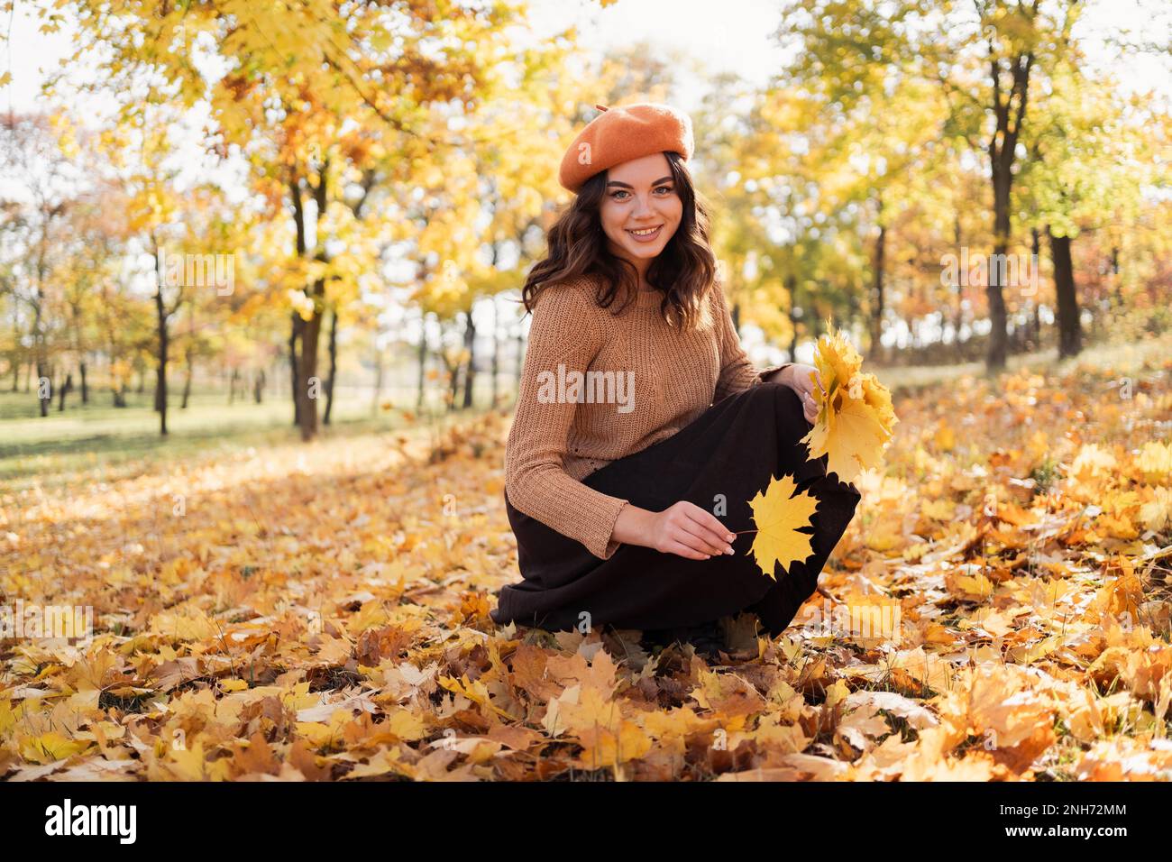 Fröhliche lächelnde junge Frau im Park auf sonnigen Herbsttagessammlungen geht. Fröhliche Frau im Pullover draußen am wunderschönen Herbsttag. Speicherplatz kopieren Stockfoto