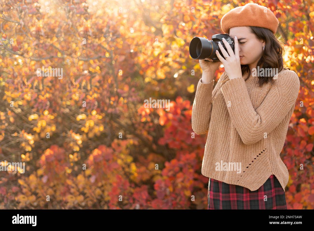 Eine wunderschöne junge Frau macht Fotos mit der Kamera in einem Wald, der das Herbstwetter genießt. Ruhe, Entspannung, Lifestyle-Konzept. Stockfoto