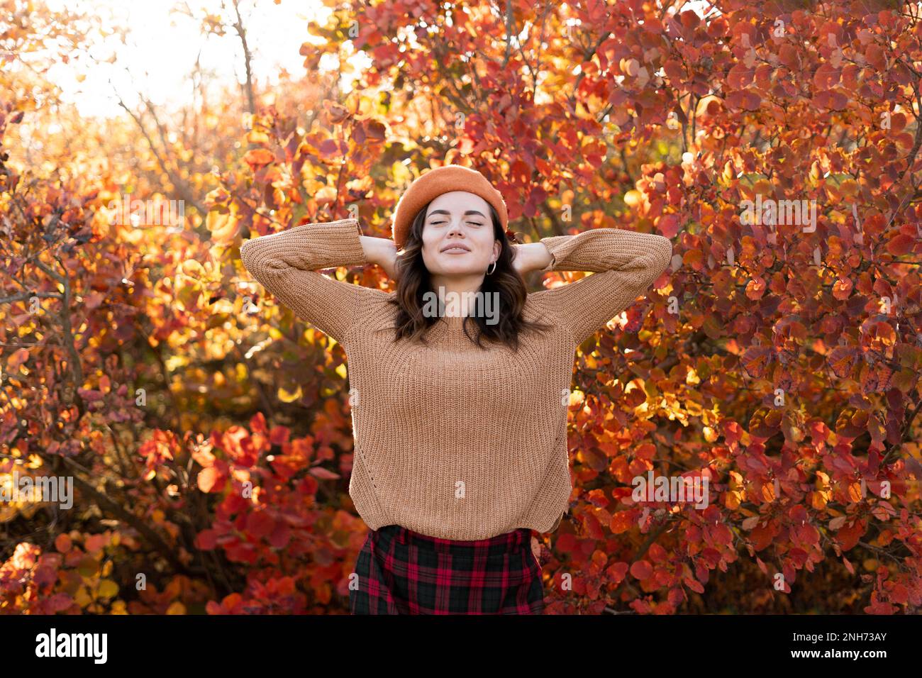 Wunderschöne junge Frau, die sich während der Herbstsaison im Park erholt. In einem Park mit rotem Laub im Hintergrund. Hübsche Frau, die es genießt, draußen Freiheit auszudrücken Stockfoto