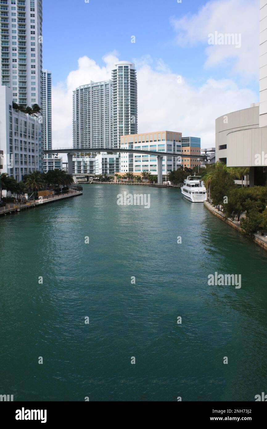 Der Miami River, der mit einem Boot, Wolkenkratzern und einem Eisenbahnsystem durch die Innenstadt von Miami fließt. Stockfoto