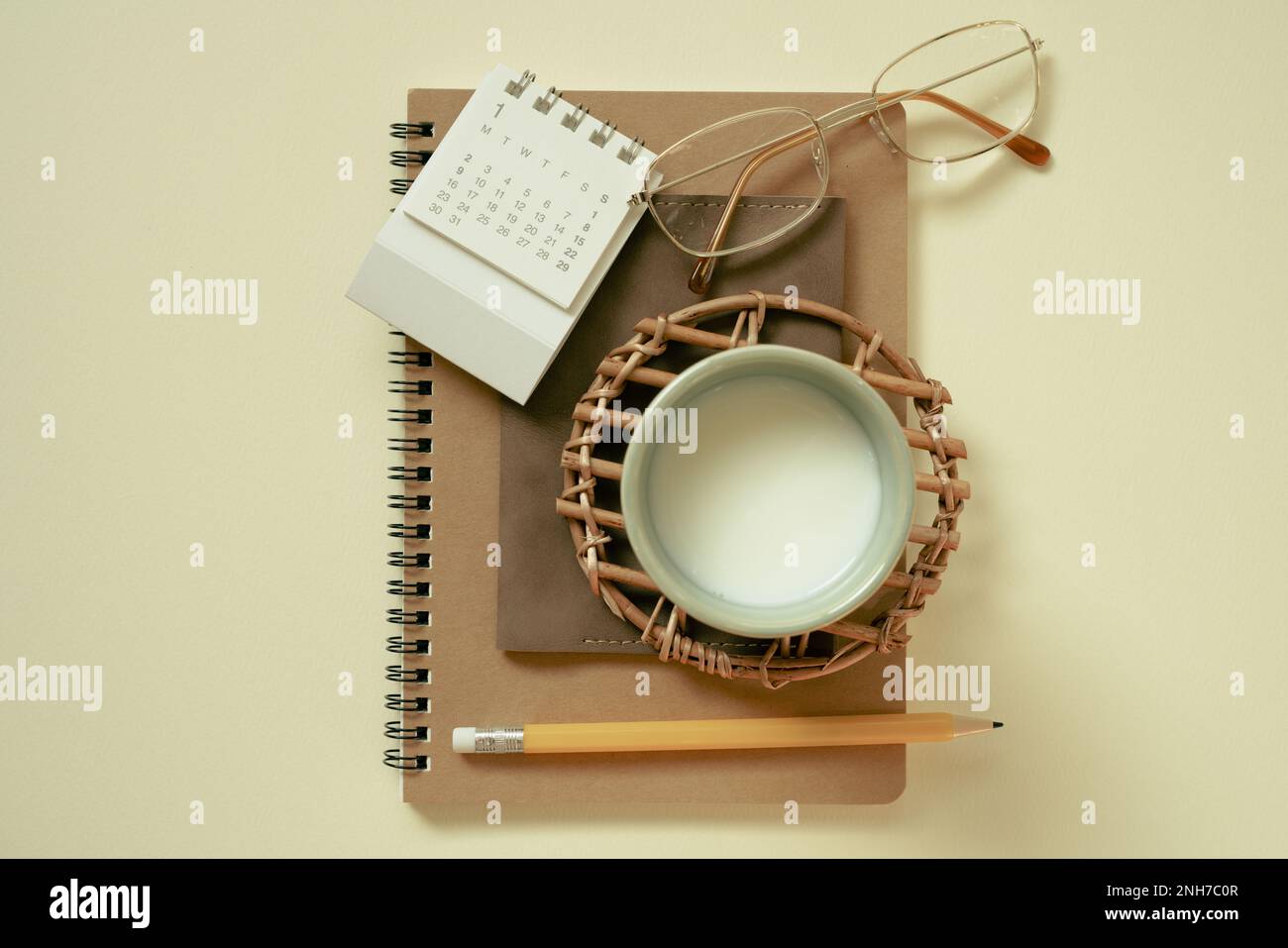 Braunes Notizbuch, Kalender, Brille, Tasse Milch, Bleistift auf gelbem Schreibtischhintergrund. Flach liegend, Draufsicht Stockfoto