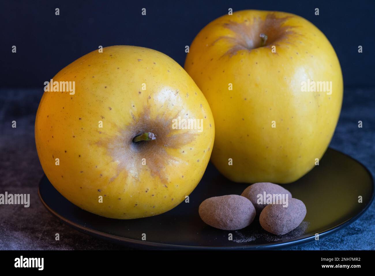 Zwei kräftige gelbe Äpfel vor dunklem Hintergrund. Stockfoto