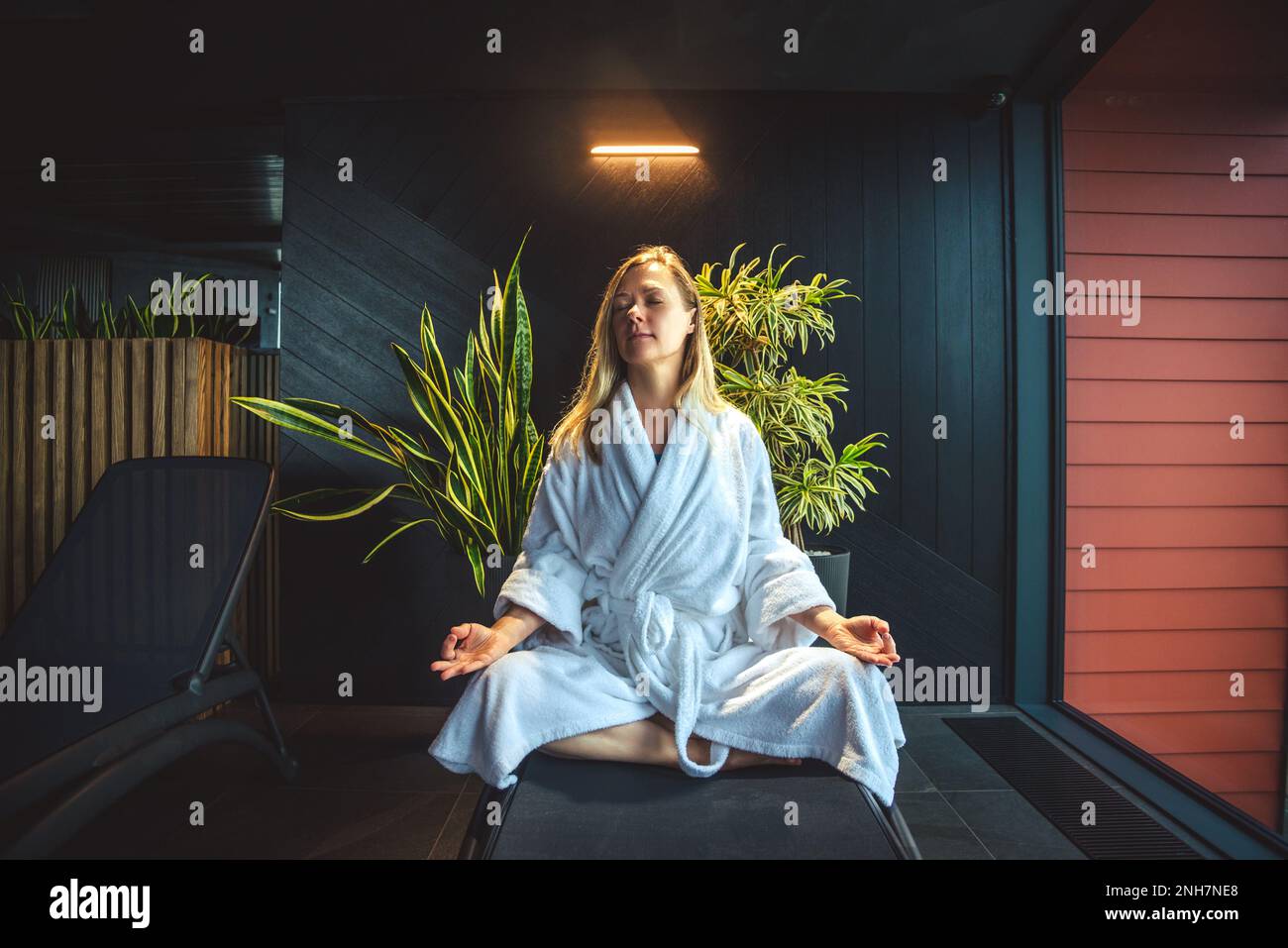 Frau im weißen Bademantel meditiert auf dem Sofa und entspannt sich zu Hause. Stockfoto