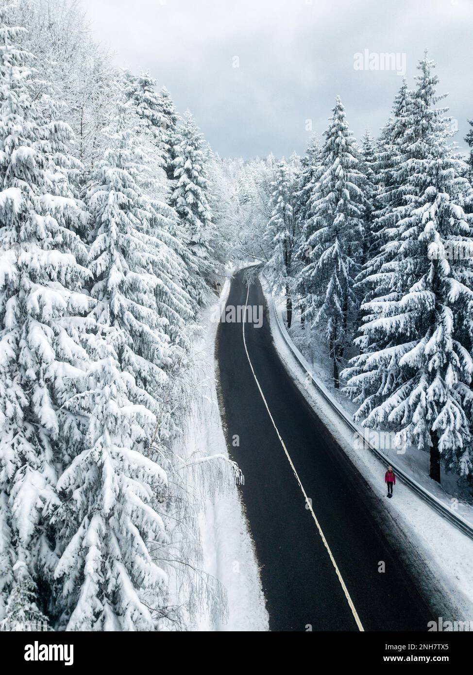 Verschneite Winterstraße in den Bergen. Aus der Vogelperspektive auf einen wunderschönen schneebedeckten Wald und eine Wanderer auf der Straße. Reisekonzept. Stockfoto