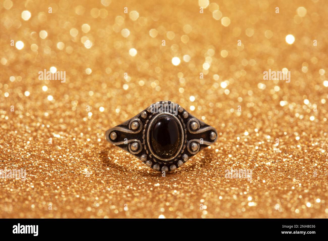 Silberring mit schwarzem Stein auf goldenem Hintergrund. Stockfoto
