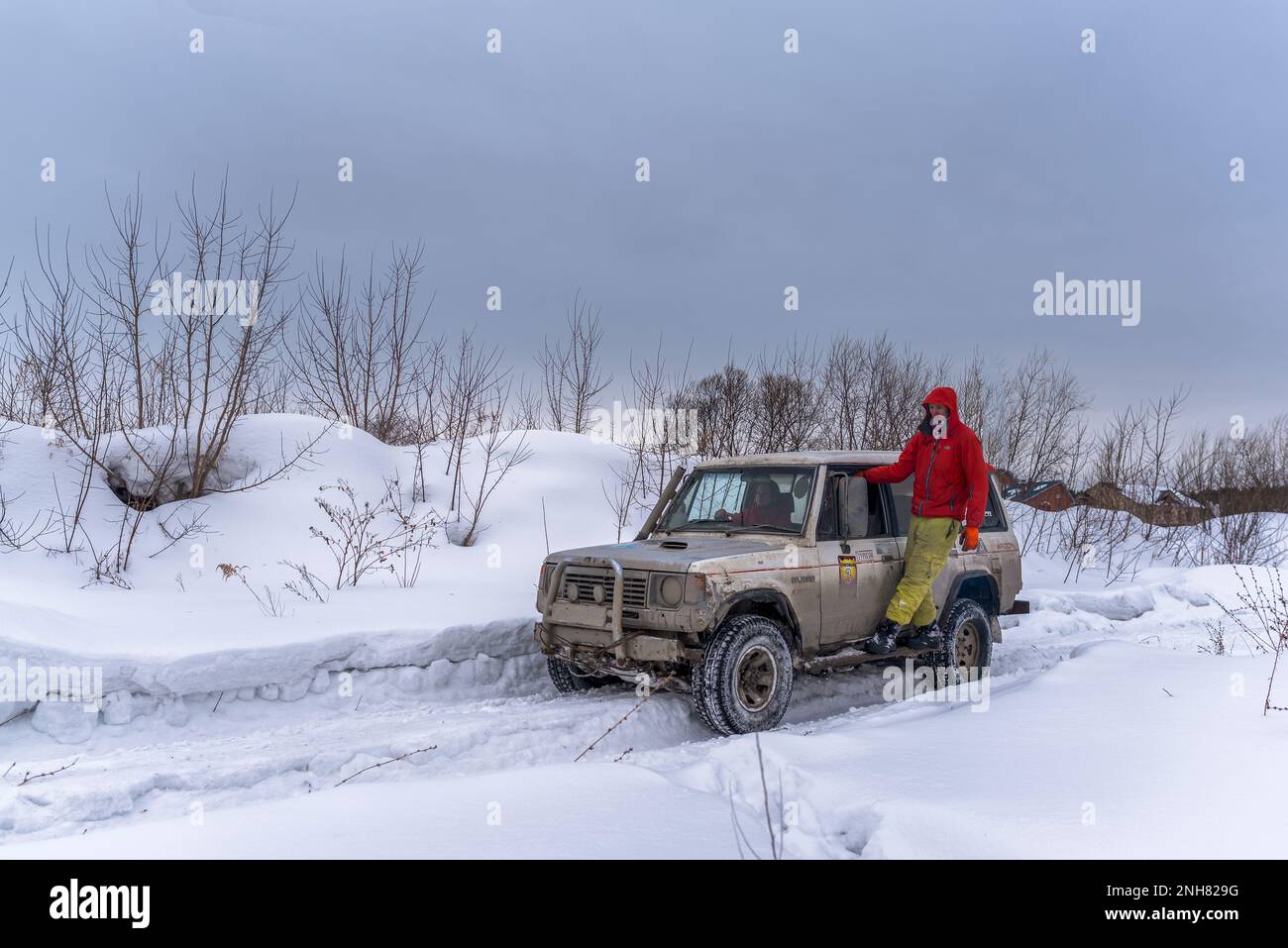 Geländewagen „Mitsubishi Pajero“ fährt im Geländewagen auf einer verschneiten Straße auf einem Feld mit einem Mann außerhalb des Körpers. Stockfoto