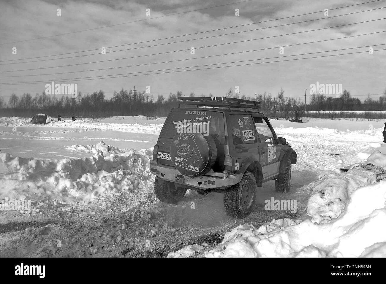 Schwarzweißfoto eines Geländewagens „Suzuki Escudo“ im Geländewagen, der schnell aktiv auf einer verschneiten Straße mit Rauchwolken im Winterfeld fährt. Stockfoto