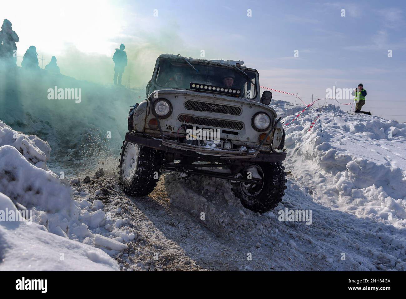 Der russische SUV „UAZ Hunter 469“ 4x4 fährt schnell und dreht die Reifen auf einer schwierigen Straße im Schnee im Winter in farbigem Rauch. Stockfoto