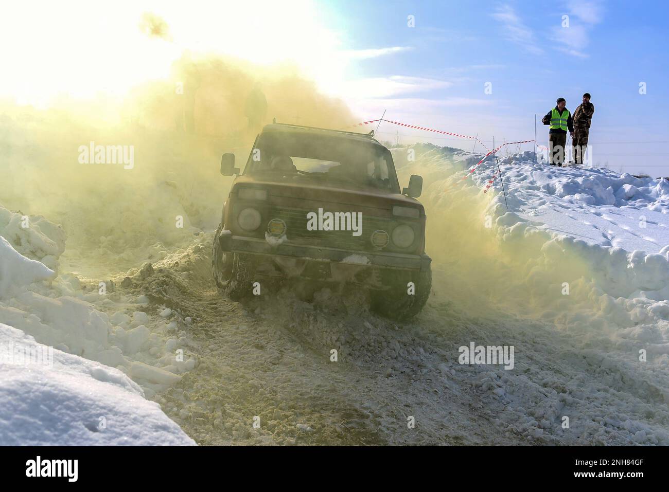 Russischer Geländewagen „Lada Niva 4x4“ fährt schnell mit einem Schneesturm durch den Schnee im Winter in gelbem Rauch im Schatten Stockfoto