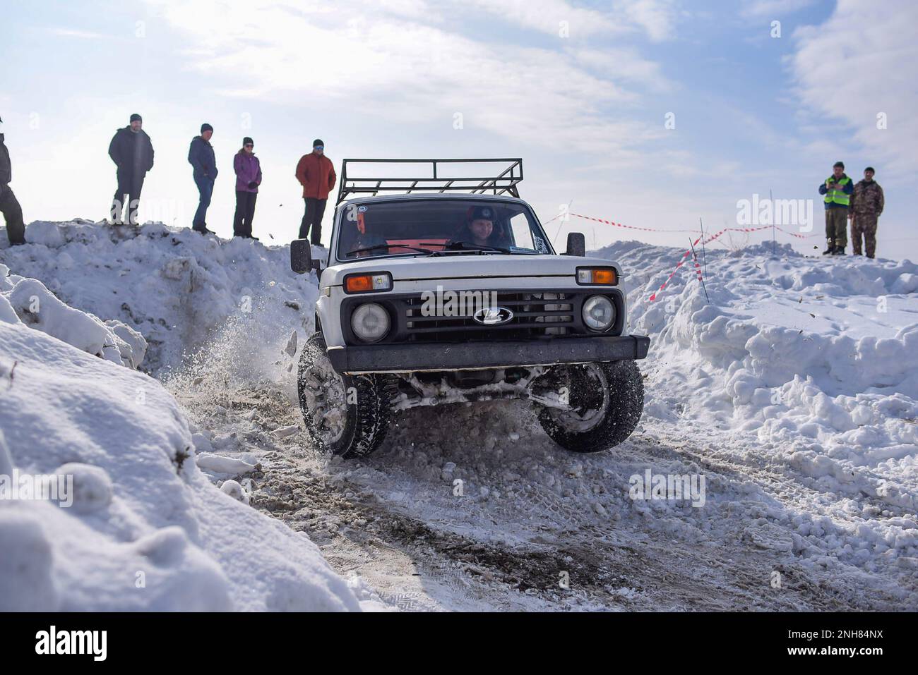 Russischer Offroad-Geländewagen „Lada Niva 4x4“ mit schnellem Schneesturm, der im Winter mit einem fröhlichen Fahrer in einem Hut mit Ohrenschützern durch den Schnee fährt. Stockfoto